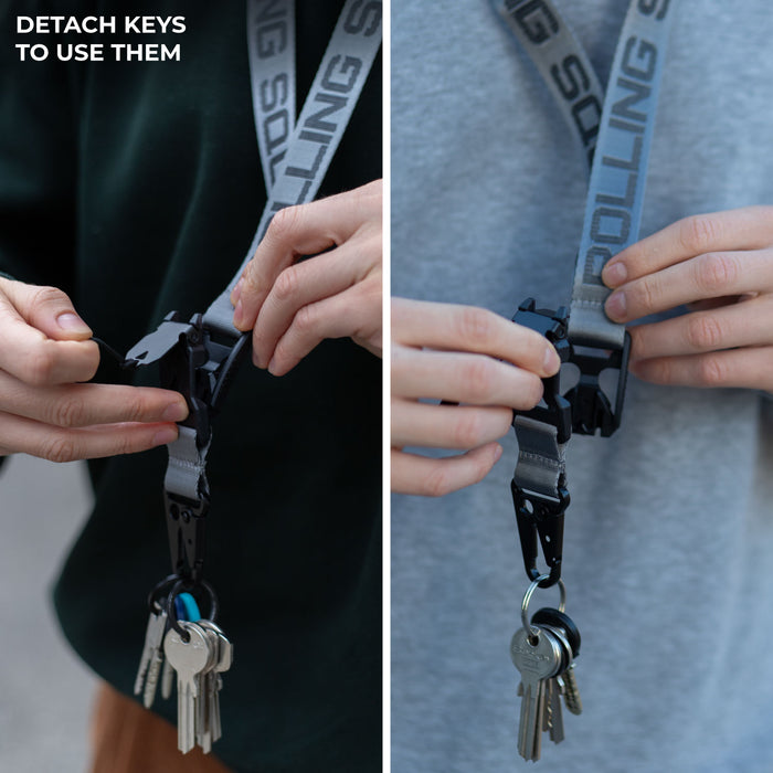Rolling Square Lanyard - Digital ID & QR Lost Mode - Rolling Square Lanyard - Digital ID & QR Lost Mode - Silver Fog - Two hands detaching black Rolling Square lanyard with white logo and keys attached, shown on gray and dark green shirts. - Rolling Square Rolling Square Lanyard - Digital ID & QR Lost Mode - Silver Fog - Two hands detaching black Rolling Square lanyard with white logo and keys attached, shown on gray and dark green shirts. - Rolling Square