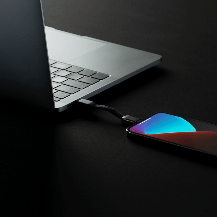 inCharge® Mini - The Smallest cable ever - USB to Lightning - Compact black USB-C to Lightning charging cable connected between a silver laptop and a smartphone with a colorful screen on . - Rolling Square