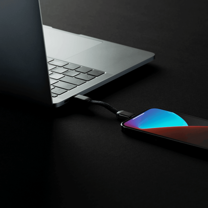 inCharge® Mini - The Smallest cable ever - USB to Lightning - Compact black USB-C to Lightning charging cable connected between a silver laptop and a smartphone with a colorful screen on . - Rolling Square