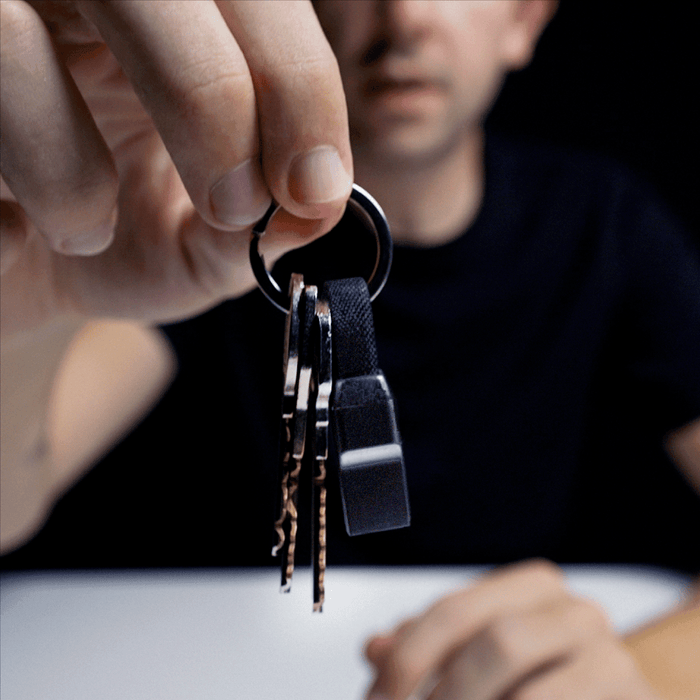 inCharge® Mini - The Smallest cable ever - USB to Lightning - Compact black charging cable attached to keyring held by a hand against a dark background. - Rolling Square